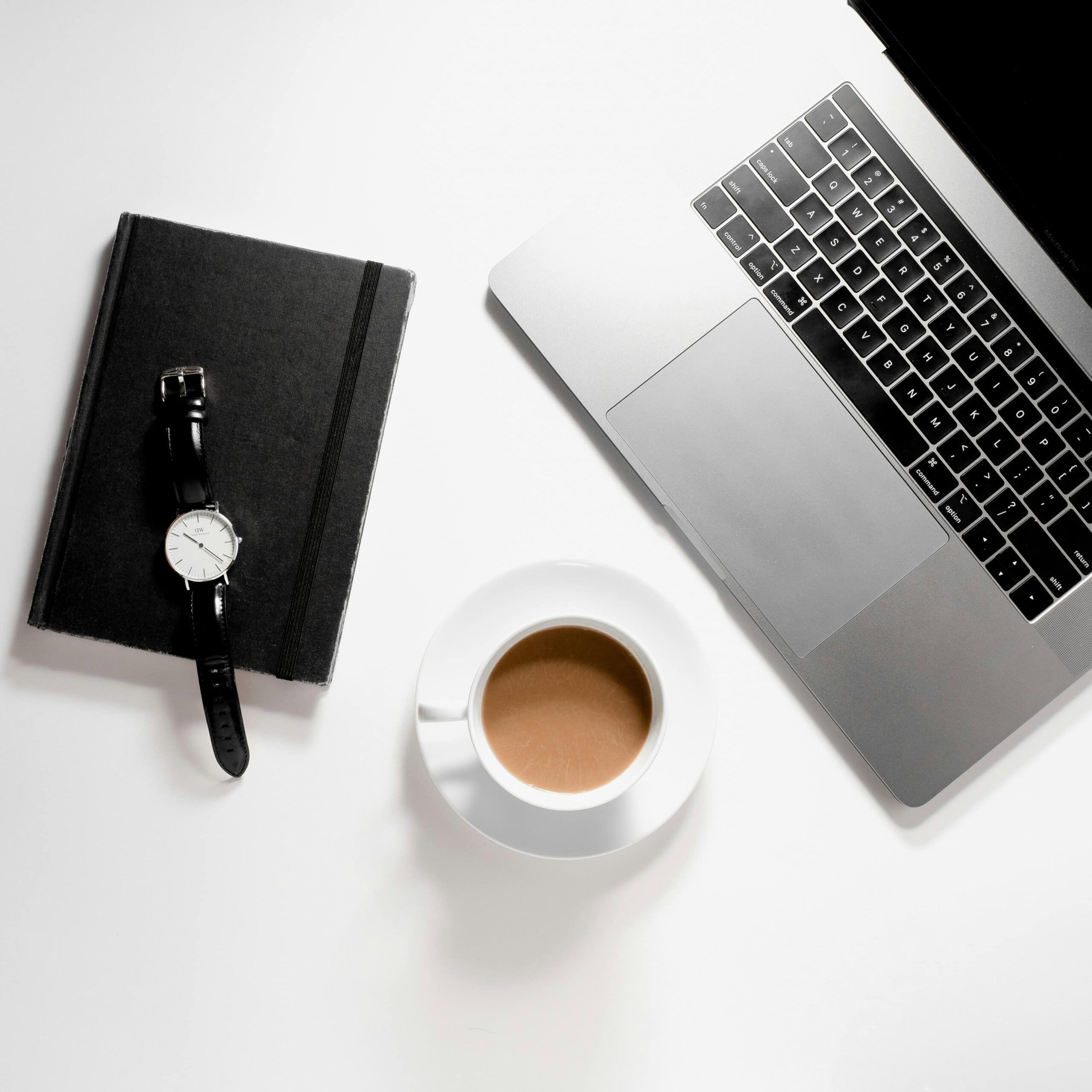 Services A watch, notebook, coffee cup, and a laptop on a white desk, symbolizing HR consulting