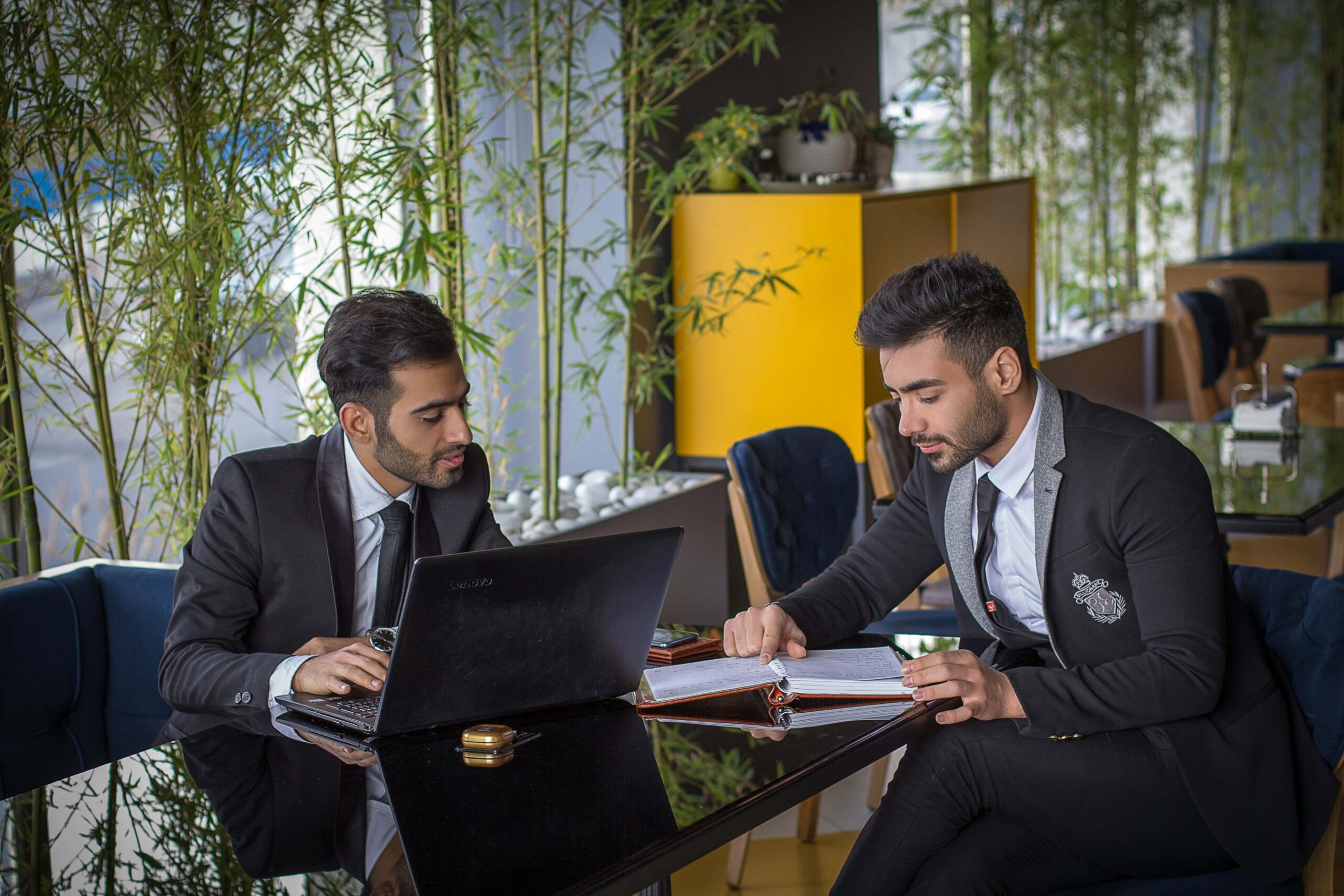 Two men in suits collaborating on a laptop in a business setting, representing professional HR consulting and business plan development.
