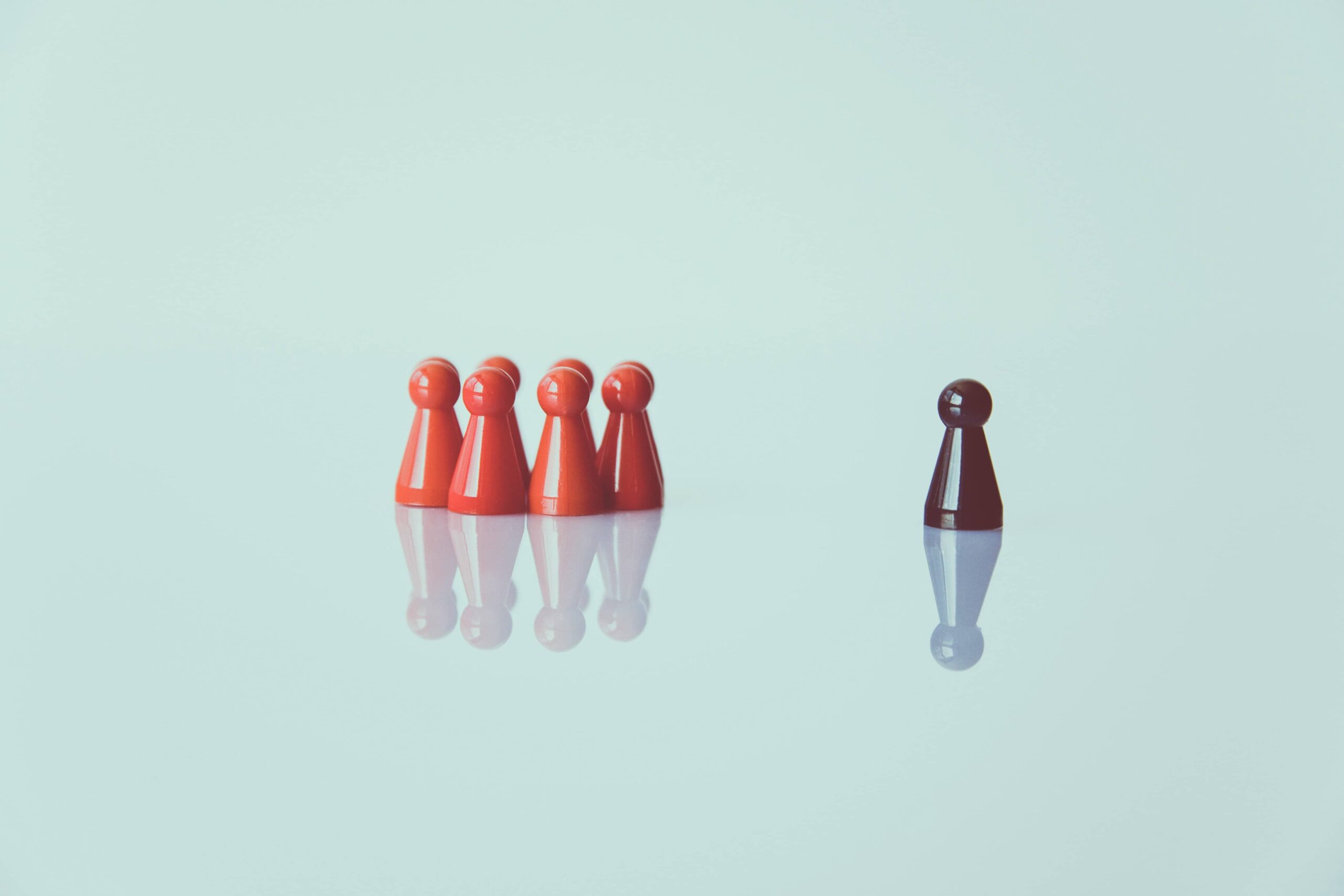 A black pawn piece standing apart from a group of red pawn pieces, a visual metaphor for leadership and effective HR consulting.