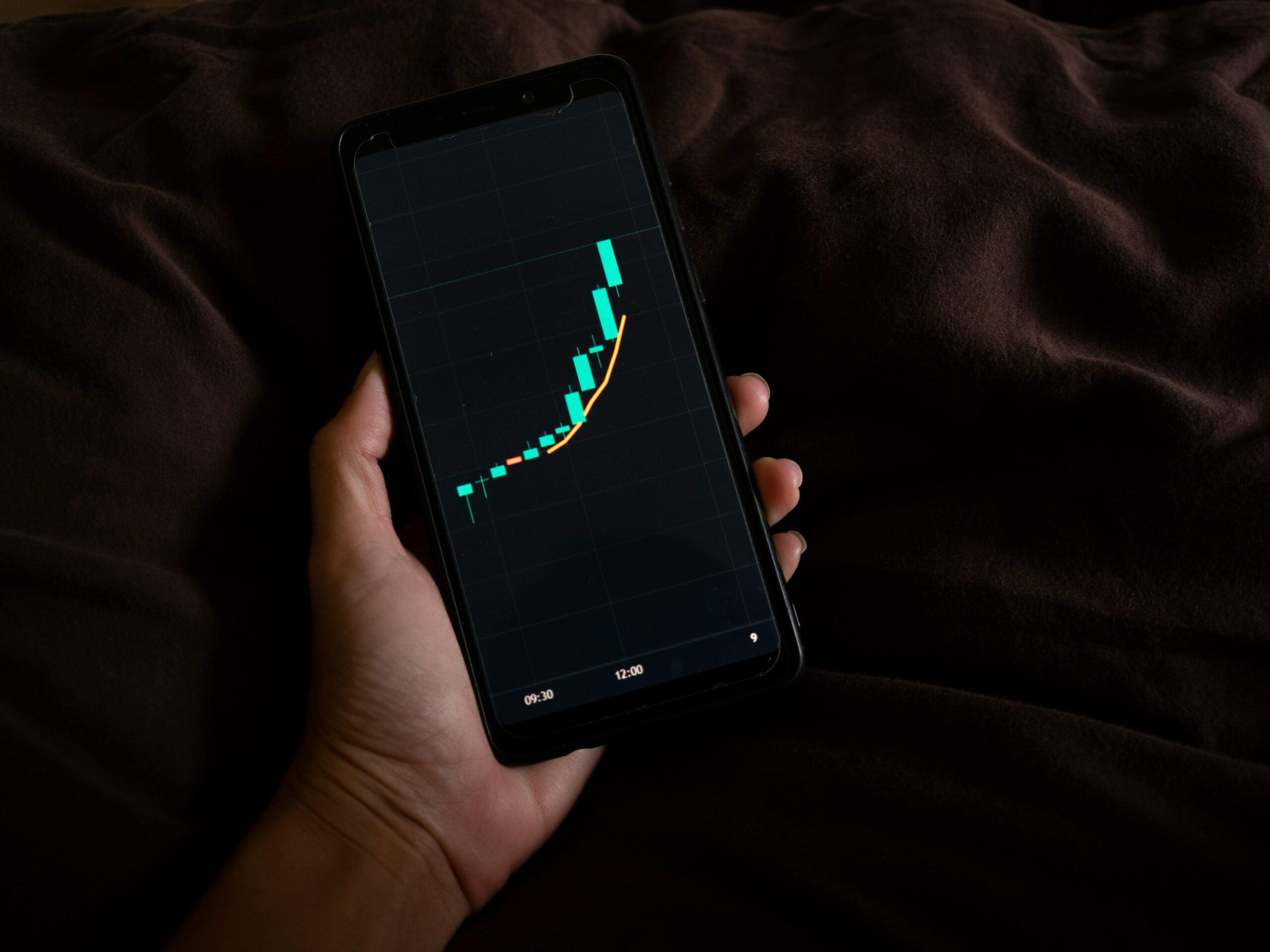 A hand holding a smartphone showing a rising financial graph, symbolizing successful business growth and strategic planning.
