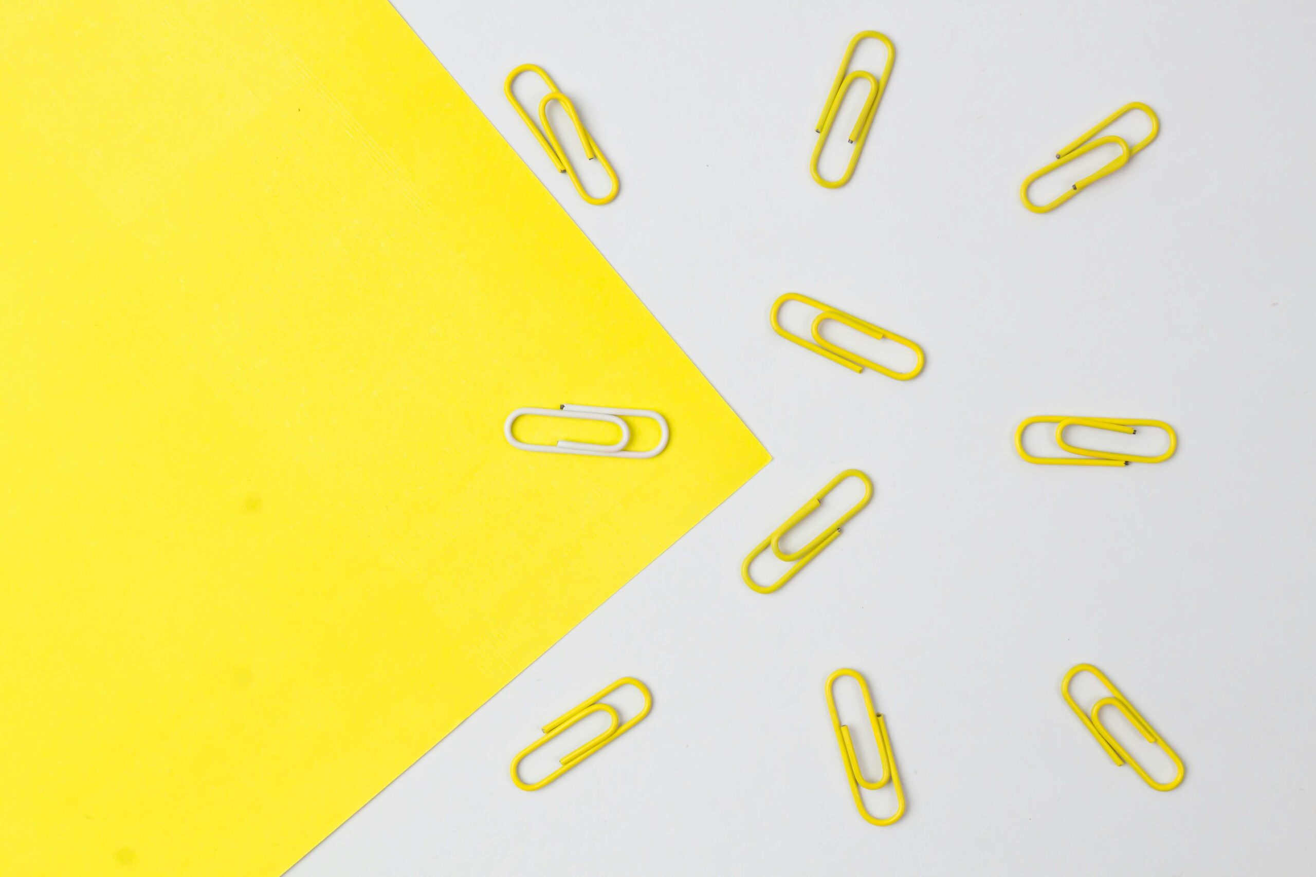 A pattern of scattered yellow paper clips on a yellow and white background, representing organization and effective HR management training.